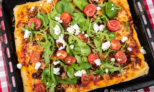 Pizza bakad i långpanna toppad med ruccola, tomat och fetaost