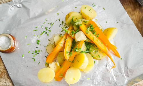Lägg kokta delad potatis och morötter på ett folieark med olivolja i botten, salta och peppra samt toppa med smör och hackad gräslök. Vik ihop och värm på grillen. 