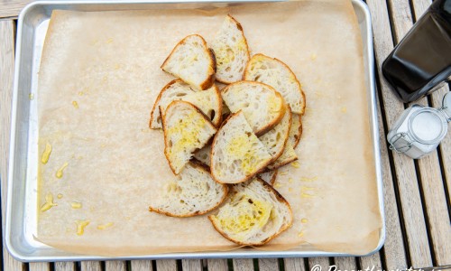 Skivat surdegsbröd blandas med olivolja samt flingsalt på bakplåtspapper.