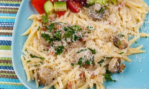 Trofie pasta med bacon, svamp och grädde på tallrik med sallad och riven parmesan. 