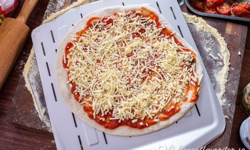 Pizzan bakas med tomat- pizzasås och riven vegan ost. 