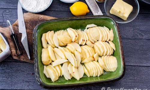 Skär äpplena i tunna skivor och placera i botten på en pajform smord med lite smör. 