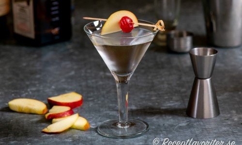 Appletini serverad i martiniglas med en skiva äpple och cocktailbär. 