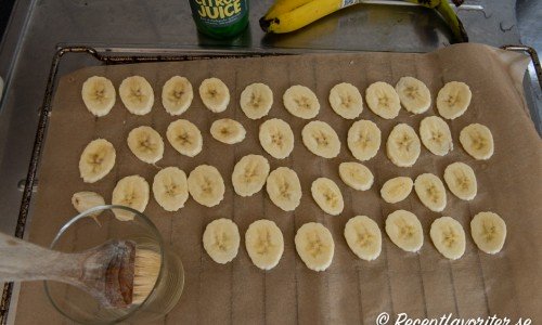 Skivad banan som penslas med citronsaft på bakplåtspapper 
