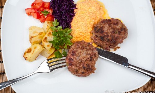 Biff a la Lindström kan serveras med valfria tillbehör - här med rostad potatis, tärnade tomater, riven rödkål och en tzatziki med riven morot. 