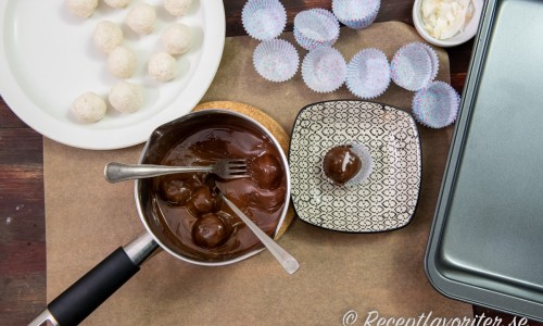 Frys kokosbollarna och doppa dem sedan i smält choklad samt lägg i knäckformar eller på bakplåtspapper att stelna. 