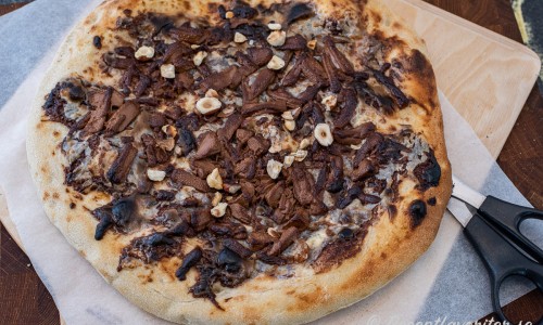 Först gräddas pizzan med enbart crème fraiche och nutella. Strö sedan över riven choklad och grädda några sekunder tills den smält och fått färg. Strö över rostade nötter och lägg på banan. 