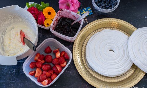 Ingredienser till marängtårtan: Vispad grädde, jordgubbar, blommor, sylt, blåbär samt marängbottnar. 