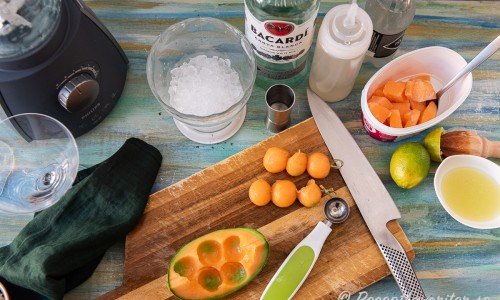 Ingredienser till fryst daiquiri med melon: krossad is, sockerlag, vichyvatten, ljus rom, fryst melon, färskpressad lime och garnering med bollar av melon på bambupinnar. 