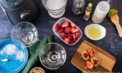 Ingredienser till jordgubbsmargaritan: frysta jordgubbar, limesaft, sockerlag, vichyvatten, krossad is, agaveessens samt apelsinliköressens. Vidare garnering av lime, cocktailbär och jordgubbshalva på bambupinne. 