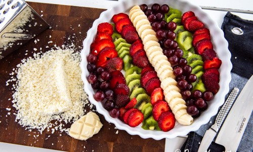 Bär och frukt till ginon lagd i mönster i en ugnssäker form med riven vit choklad bredvid. 