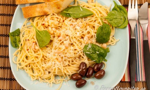 Heta räkor med pasta på tallrik med oliver, basilika och bröd till. 