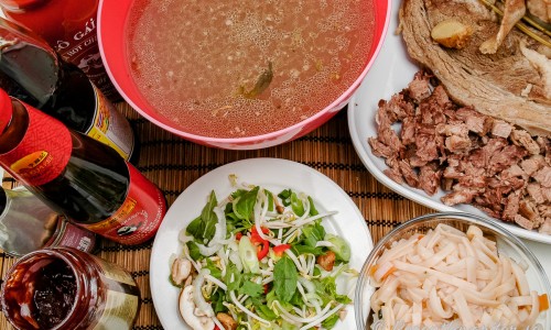 Silad köttbuljong smaksätts med soja, lime med mera; vidare grönsaker och örter; kokta nudlar och kött till soppan. 