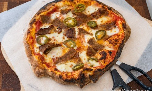 Kebabpizza bakad i pizzaugn serverad på bakplåtspapper med sax. 