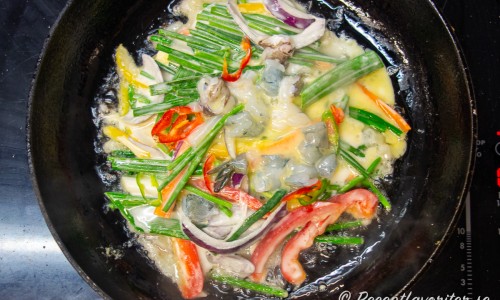 Först steks grönsakerna i smeten, sedan toppar man med skaldjur och sedan hälls uppvispat ägg på toppen. 