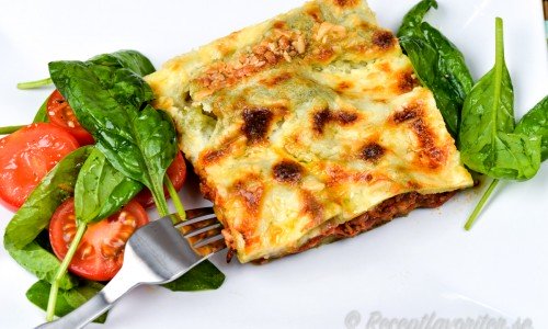 Lasagne med spenatplattor serverad på tallrik med grönsallad. 