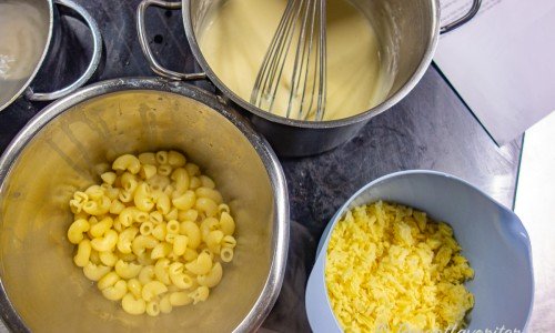 Kokta makaroner al dente, bechamelsås och riven cheddarost redo att blandas ihop. 