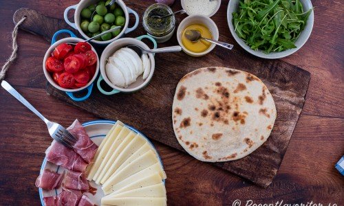 Piadina med prosciutto, pecorino, tomat, mozzarella, oliver, pesto, olivolja, balsamico, basilikakräm och ruccola. 