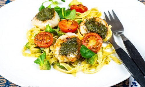 Grillade eller stekta pilgrimsmusslor toppade med pesto serverad med pasta tagliatelle, tomat, avokado och spenat. 