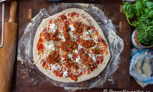 Pizzabotten toppas med tomatsås, riven mozzarella, köttfärssås samt klippt färsk rosmarin. 