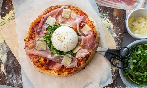 Pizza med tomatsås och mozzarella toppad med en hel burrata på rucola omgiven av prosciutto samt toppad med olivolja, svartpeppar och pecorino. 