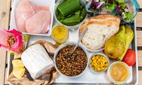 Ingredienser till salladen: kycklingfilé, valnötter, getost i rulle, citron, dressing av olivolja och äppelcidervinäger, gurka, sockerärtor, matvete, surdegsbröd, majs, grönsallad, päron, tomat och honung. 