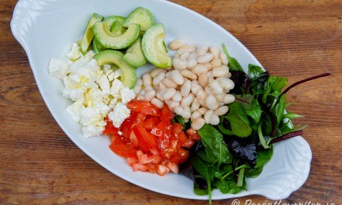 Ett fat med sallad med små vita bönor, avokado, tomat, fetaost och grönsallad.