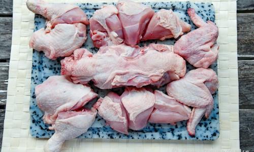 Styckad kyckling i delar på skärbräda