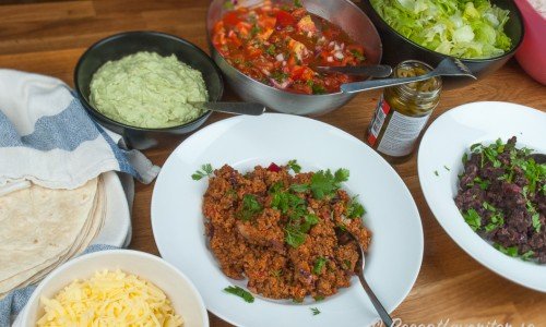 Varma tortillabröd, guacamole, tomatsalsa, isbergssallad, riven ost, tacofärs (köttfärs för de som vill ha det) och stekta mosade svarta bönor. 