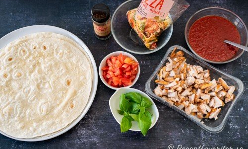 Ingredienser jag hade till min tortillapizza: stora vetetortillas, riven ost, anchochili, tärnade tomater, färsk basilika, stekt kyckling och pizzasås. 