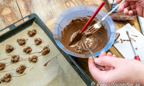 Nötterna vänds i choklad och sedan tar man upp tre åt gången och lägger i en liten hög att stelna. 