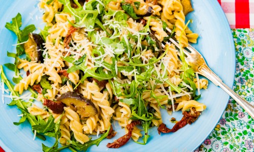Vegetarisk pasta på tallrik garnerad med riven ost och ruccola