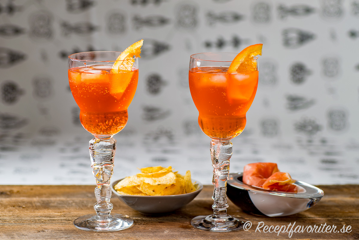 Två glas Aperol Spritz garnerade med apelsin och serverade med chips och parmaskinka. Två glas Aperol Spritz garnerade med apelsin och serverade med chips och parmaskinka.