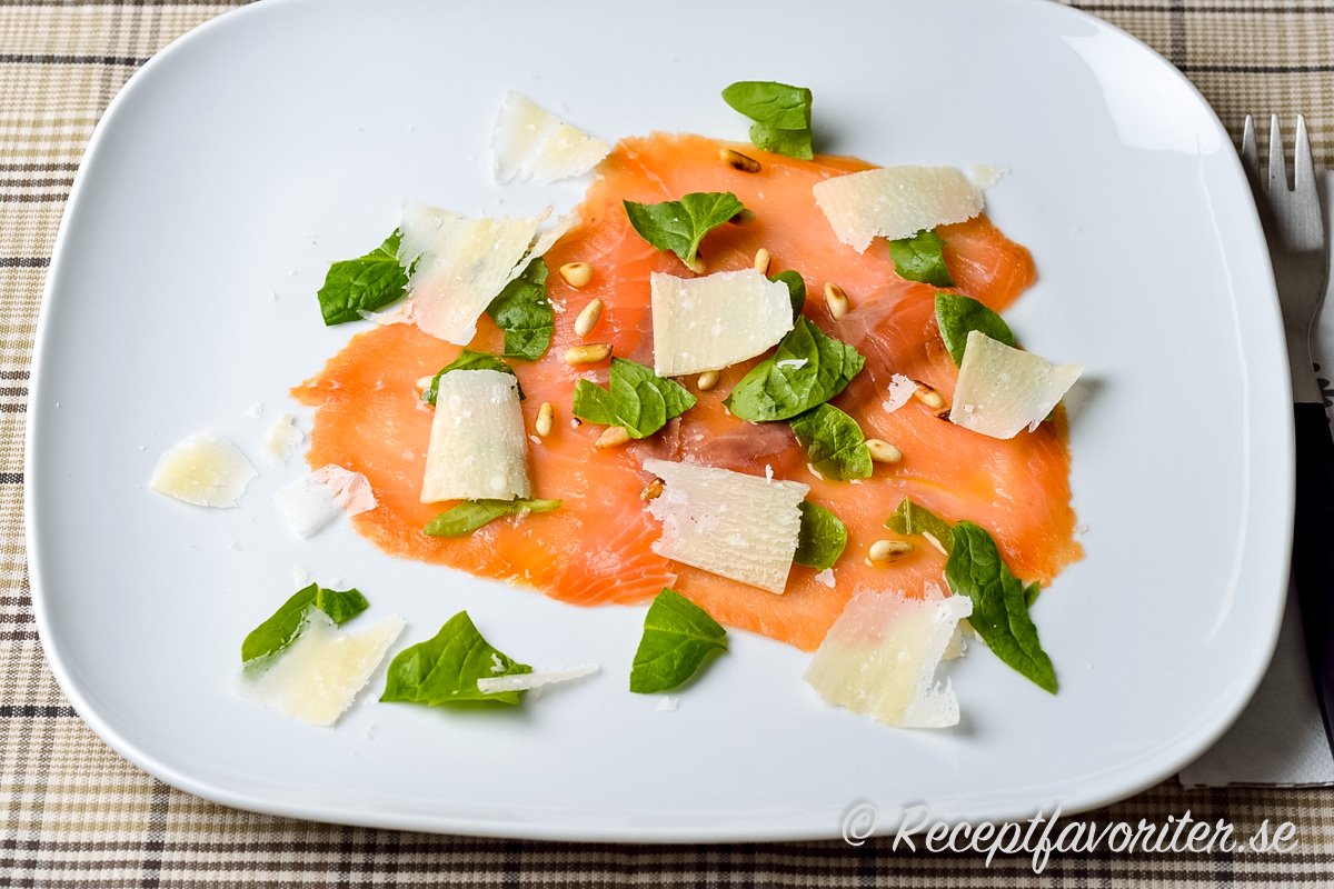 Carpaccio på lax i tunna skivor garnerad med rostade pinjenötter, hyvlad parmesan samt färsk basilika. 