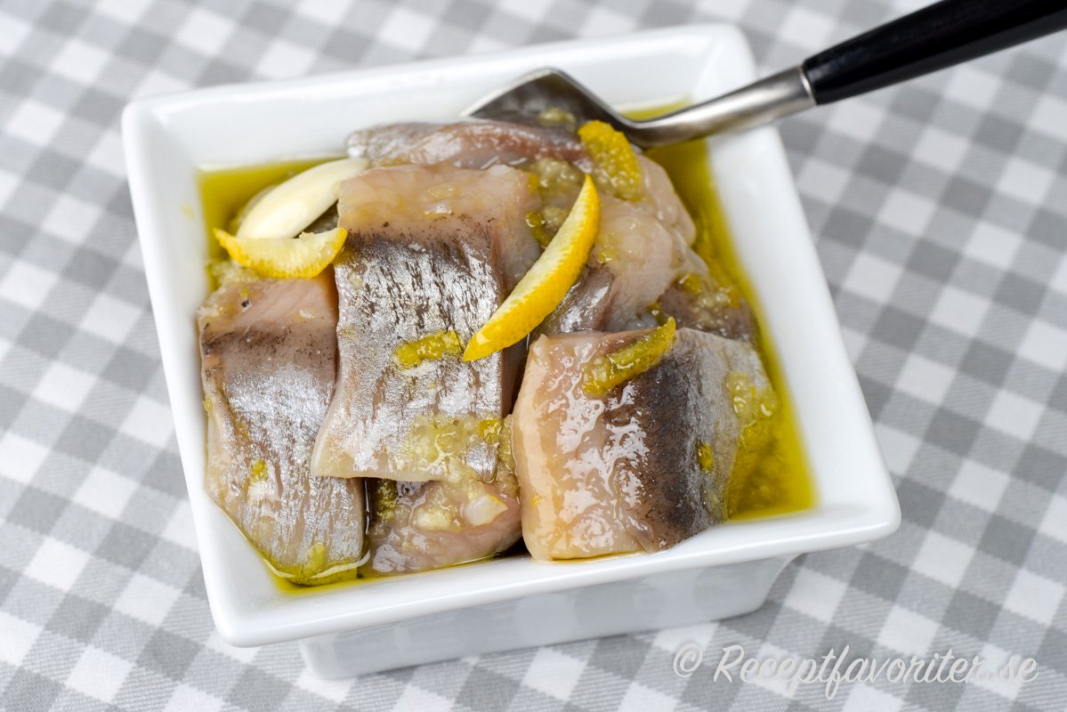 Sill inlagd med citron och vitlök i en klar lag i skål Sill inlagd med citron och vitlök i en klar lag i skål