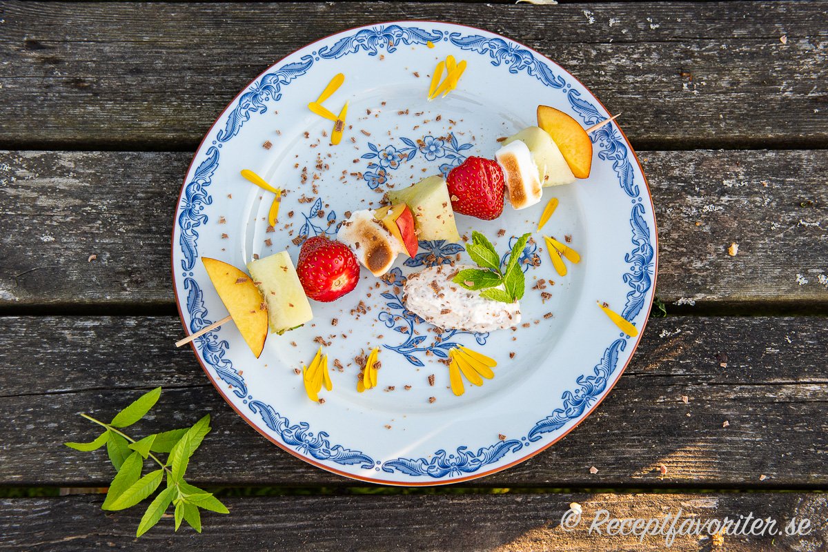 Ett fruktspett serverat med Daimgrädde, ringblomma, riven Daimchoklad, mynta samt citronverbena som garnering. Ett fruktspett serverat med Daimgrädde, ringblomma, riven Daimchoklad, mynta samt citronverbena som garnering.