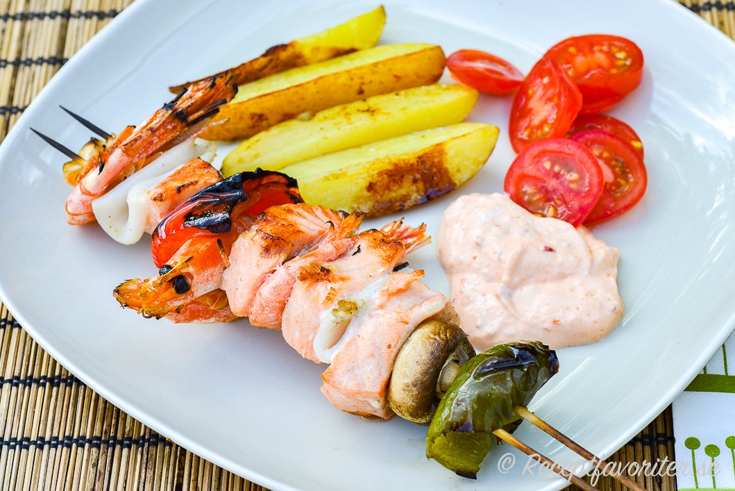 Grillspett med fisk, bläckfisk och räkor på grillen serverat med klyftpotatis och en kall sås. Grillspett med fisk, bläckfisk och räkor på grillen serverat med klyftpotatis och en kall sås.