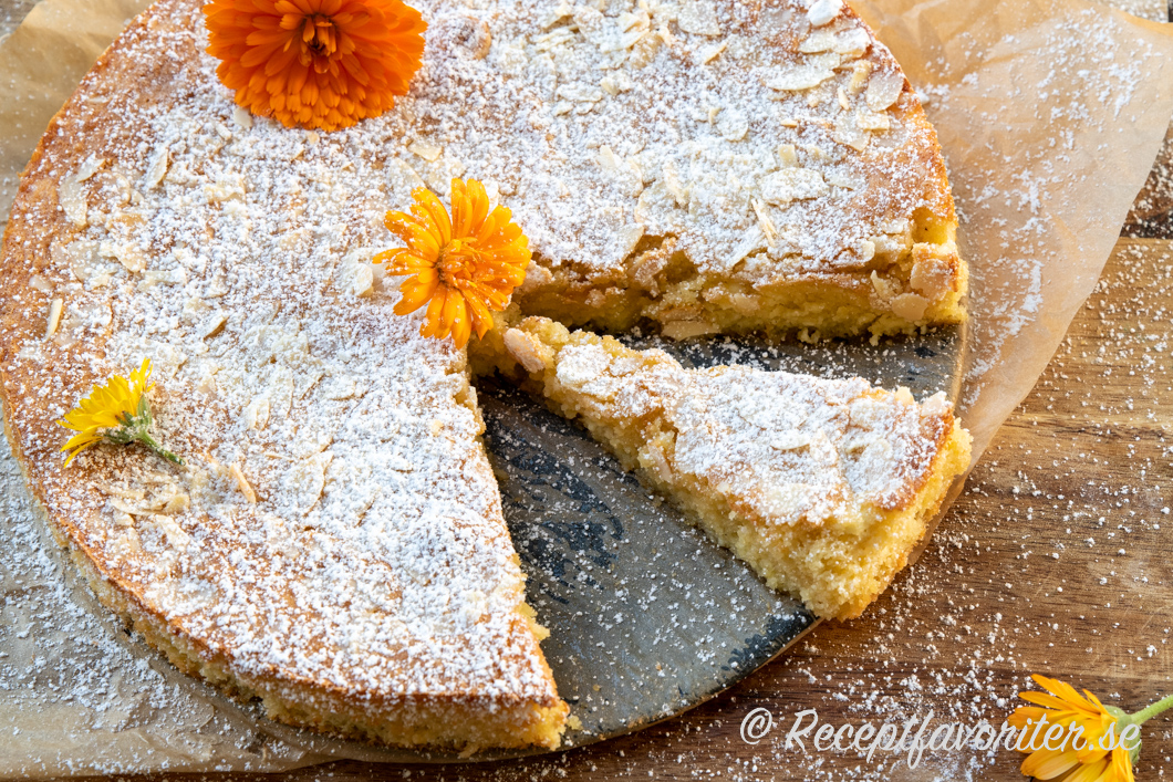 Italiensk mandelkaka med ricotta uppskuren i bit garnerad med ringblommor och florsocker. Italiensk mandelkaka med ricotta uppskuren i bit garnerad med ringblommor och florsocker.