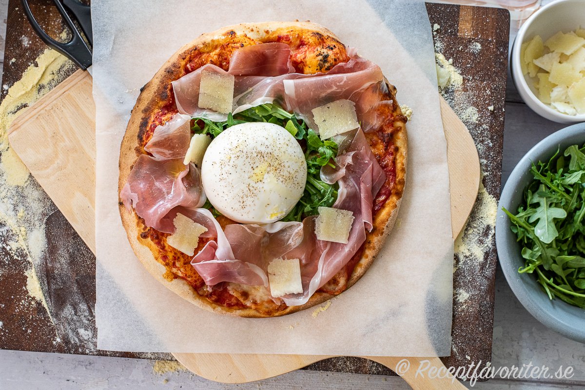 En god variant är att först baka grunden på pizzan med tomatsås och ost och sedan toppa när man tar ut den med det man gillar. Ovan med prosciutto, rucola, pecorino samt burrata med olivolja och svartpeppar. 