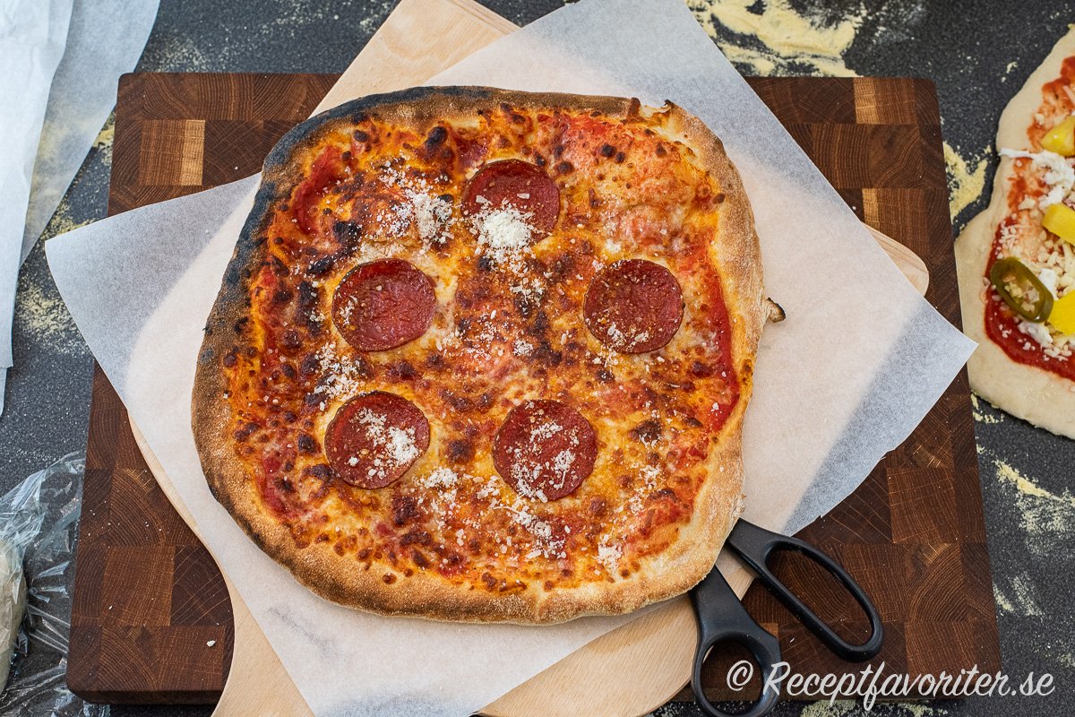 En nybakta pizza med tomat, mozzarella och pepperoni salami toppad med lite riven parmesan till servering. Kan serveras på tallrik med kniv och gaffel eller bakplåtspapper på skärbräda med sax. 
