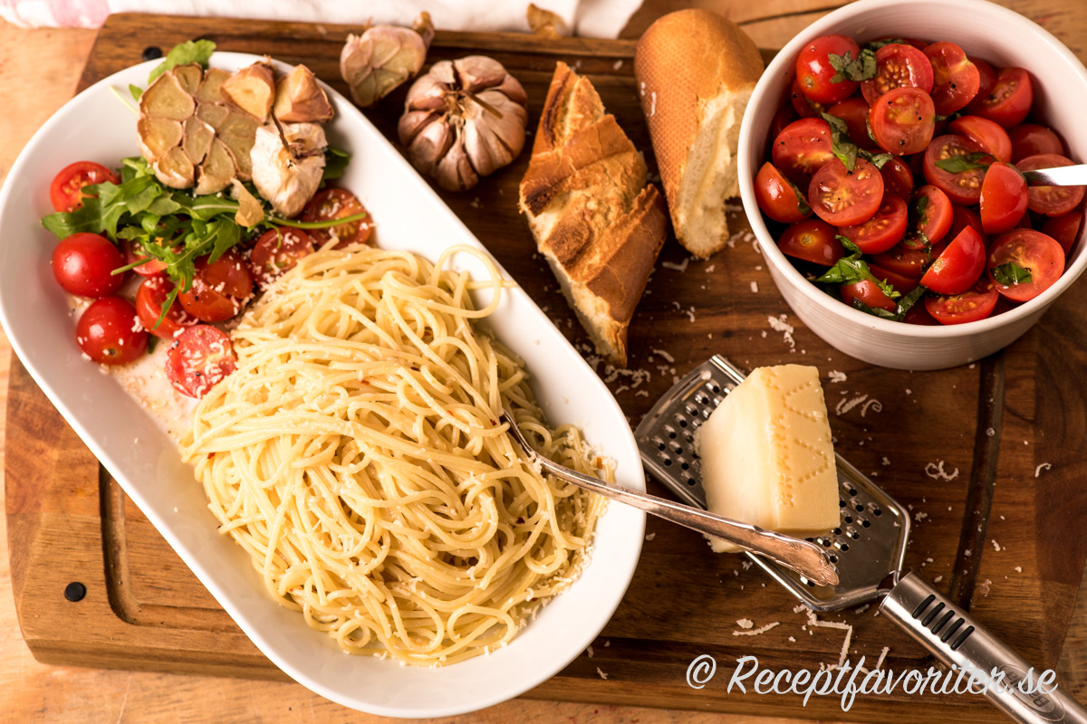 Spagetti med vitlök toppad med riven parmesan och serverad med rostad vitlök samt en enkel tomatsallad med cocktailtomater och rucola. 
