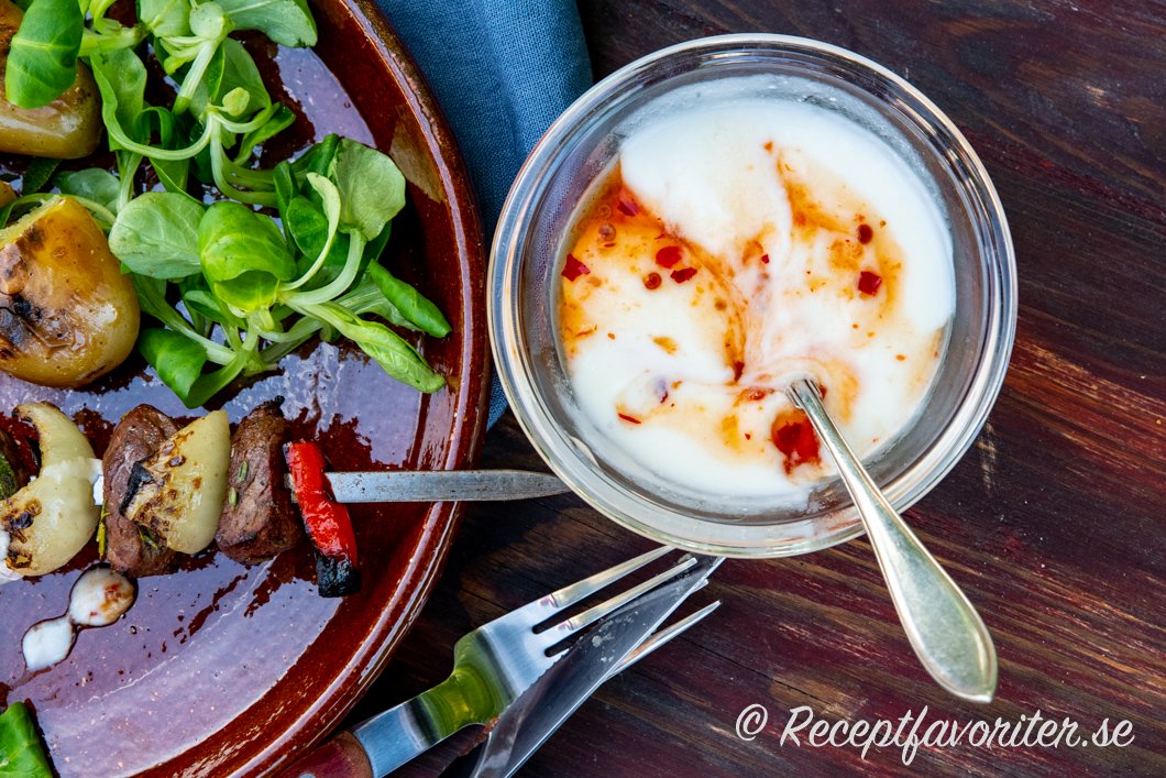 En kall sås med naturell yoghurt och het söt sweet chilisås serverad i skål till grillspett. 