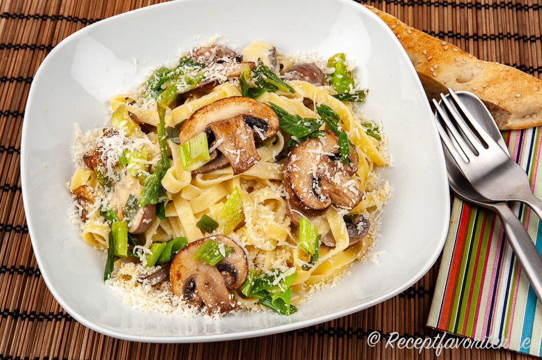 Tagliatelle med champinjoner, grädde, smör, parmesan, vitlök och salladslök i tallrik. 