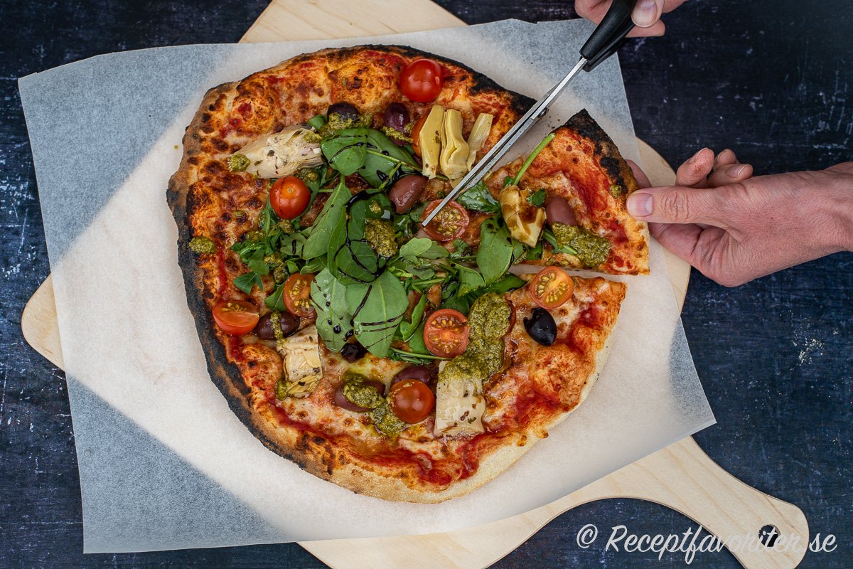 Vegopizza med tomat och ost i botten som toppas med grönt som spenat, rucola, tomater, oliver, kronärtskockor och pesto samt crema di balsamico.