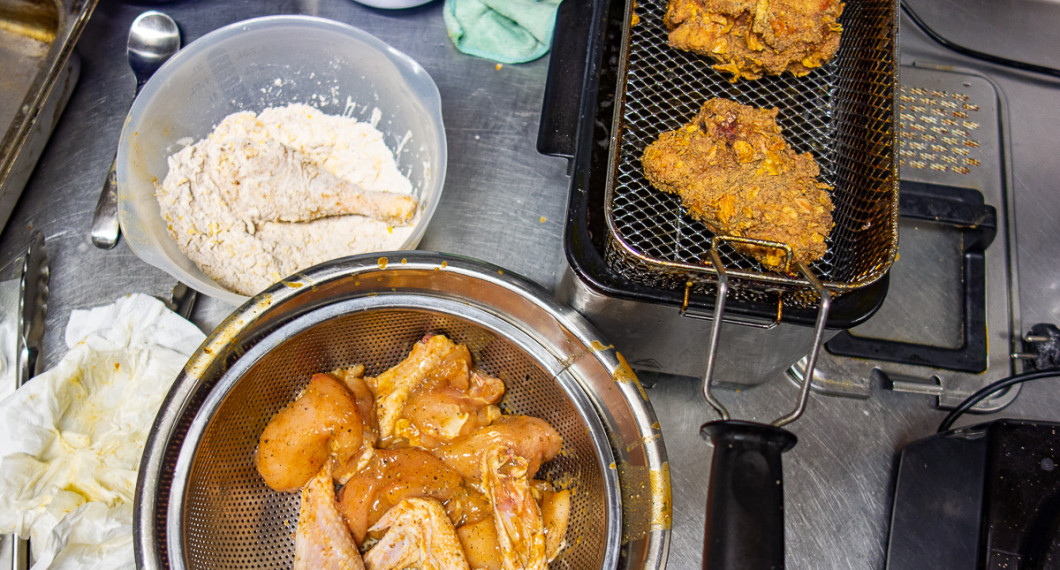 Kycklingbitarna får rinna av i ett durkslag och vänds sedan runt i paneringen innan fritering.