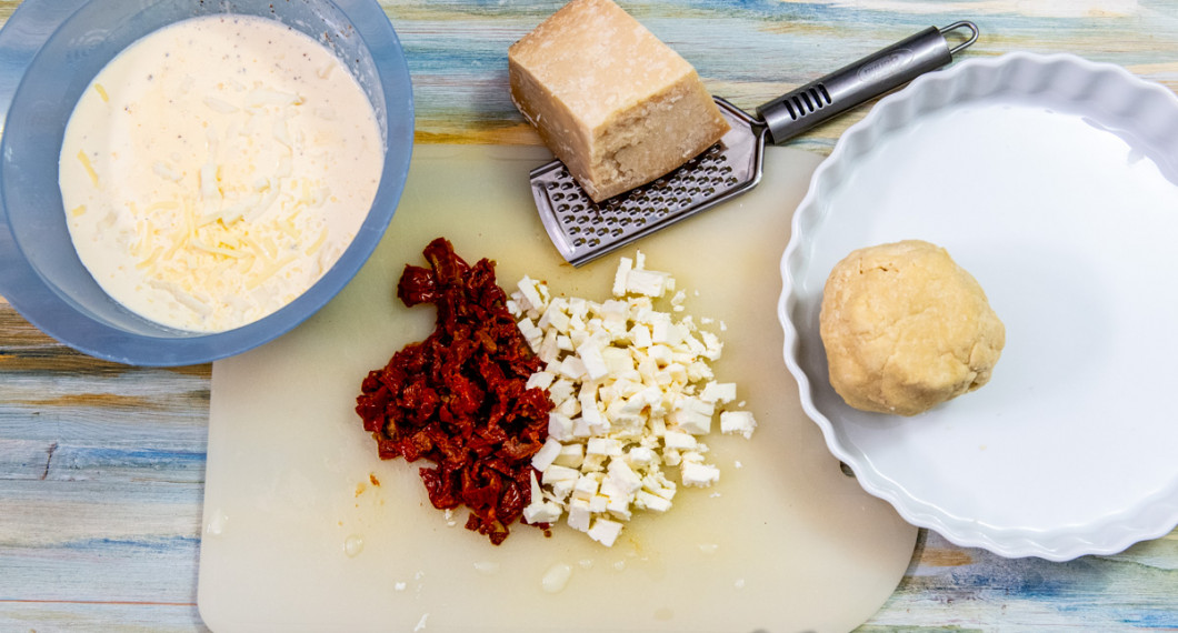 Till pajen behöver du äggstanning av grädde, ägg, riven ost och peppar; vidare soltorkade tomater, fetaost, parmesan samt pajdeg. 
