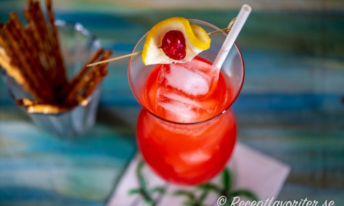 Planters Punch i högt glas med citron och marashino cocktailbär, is och drinkpinne